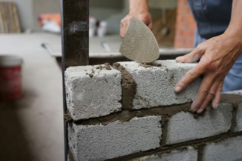 Albañil extendiendo mortero con la paleta sobre un muro de bloques de hormigón